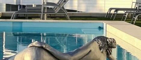 A sculpture of a reclining woman by a pool with a modern building in the background.