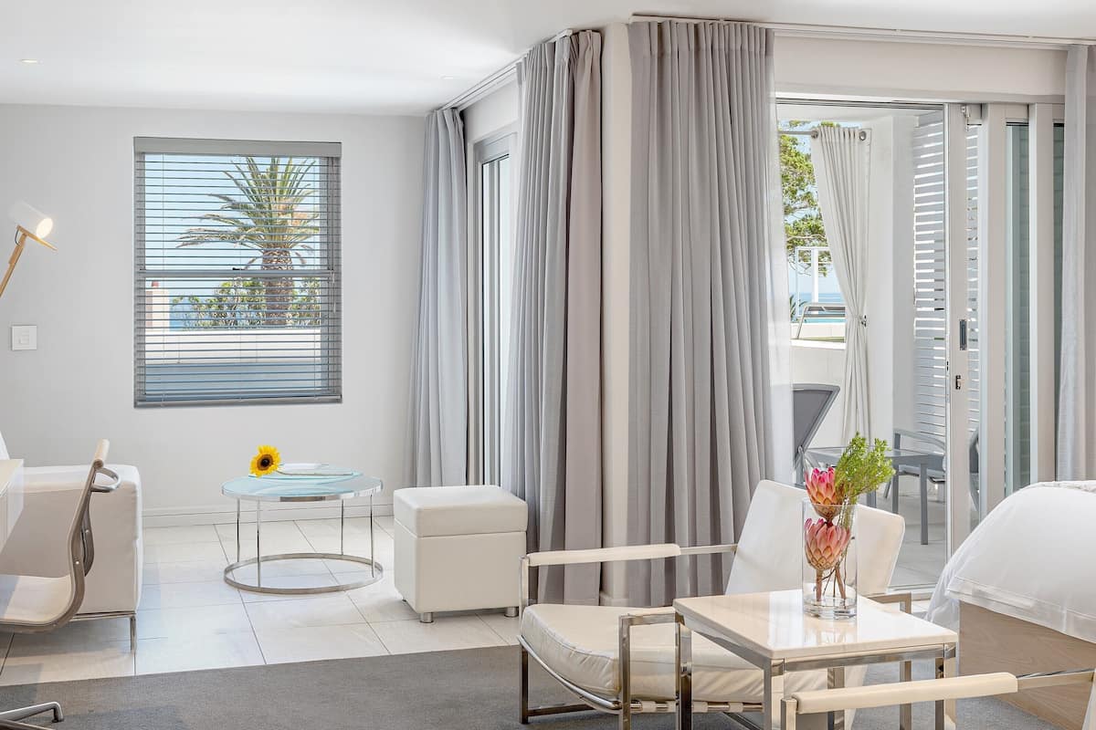 A modern hotel room with a sofa, a small round table, a glass coffee table, and a bed.