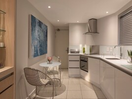 A modern kitchen with white cabinets, a stainless steel range hood, and a glass-top dining table with wire chairs.