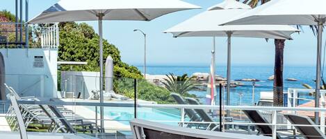 A poolside area with lounge chairs and umbrellas, overlooking a body of water and greenery.