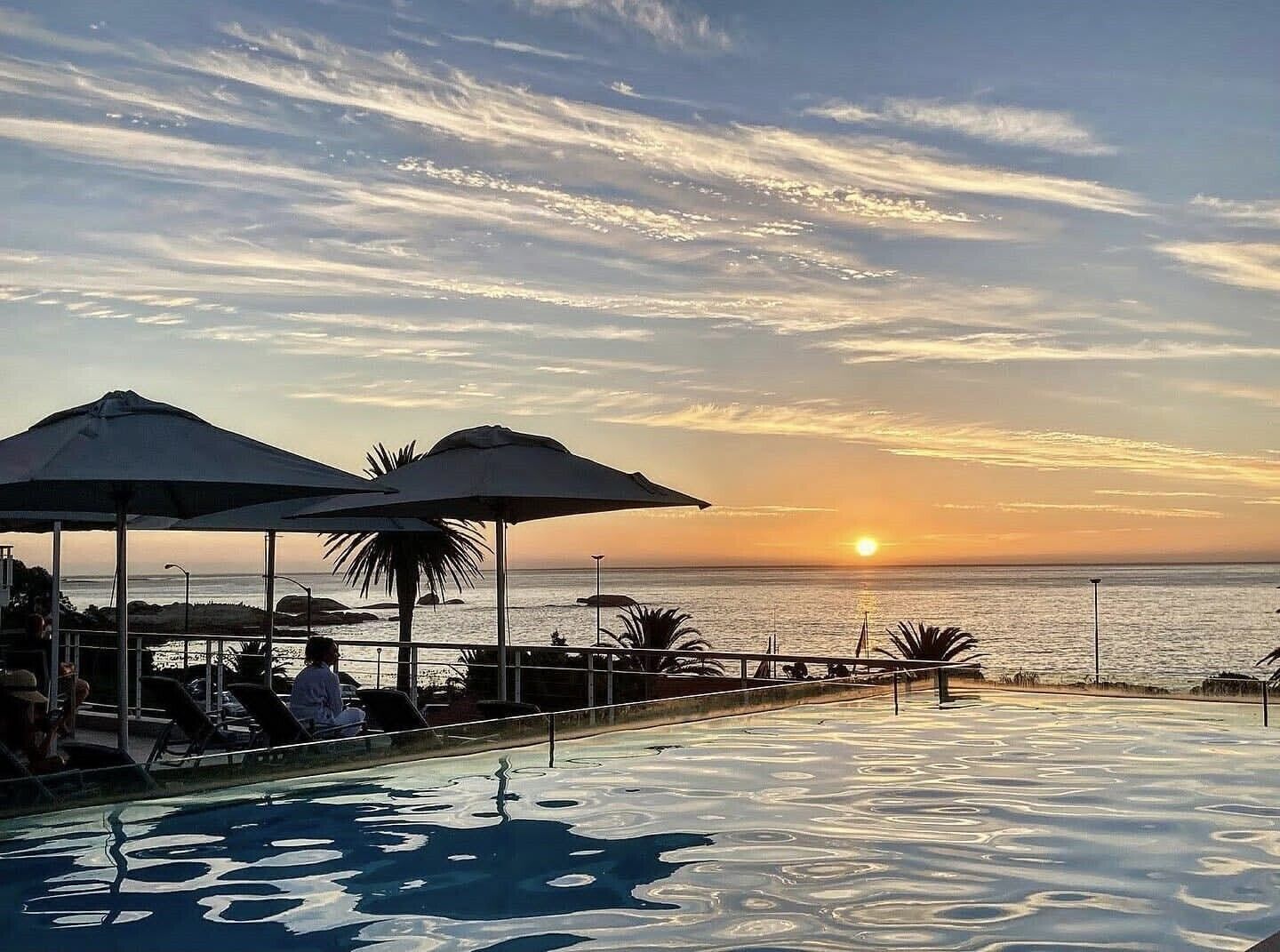 An infinity pool with a sunset view, umbrellas, and lounge chairs.