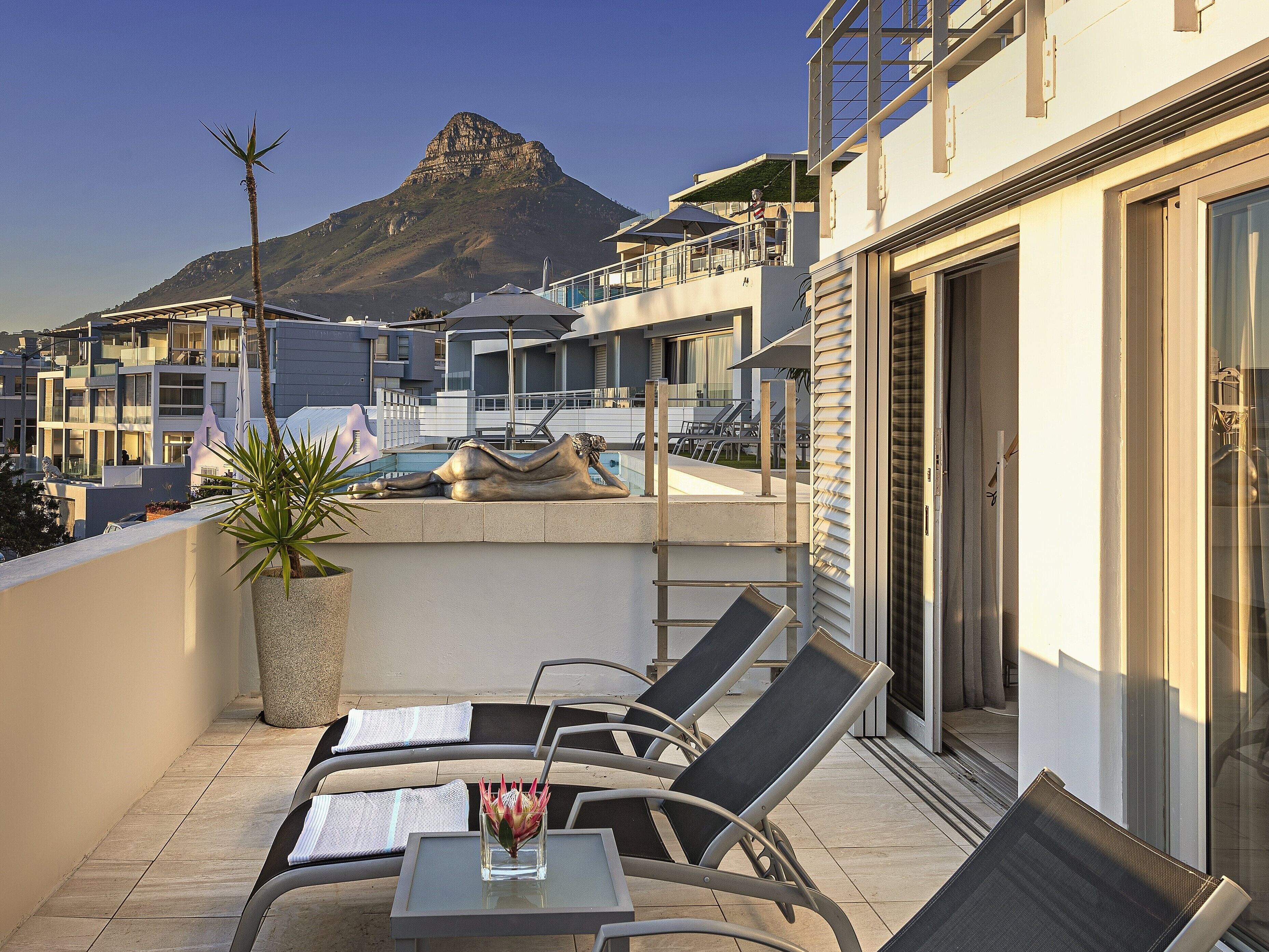 A rooftop terrace with lounge chairs, a small table, and a statue.