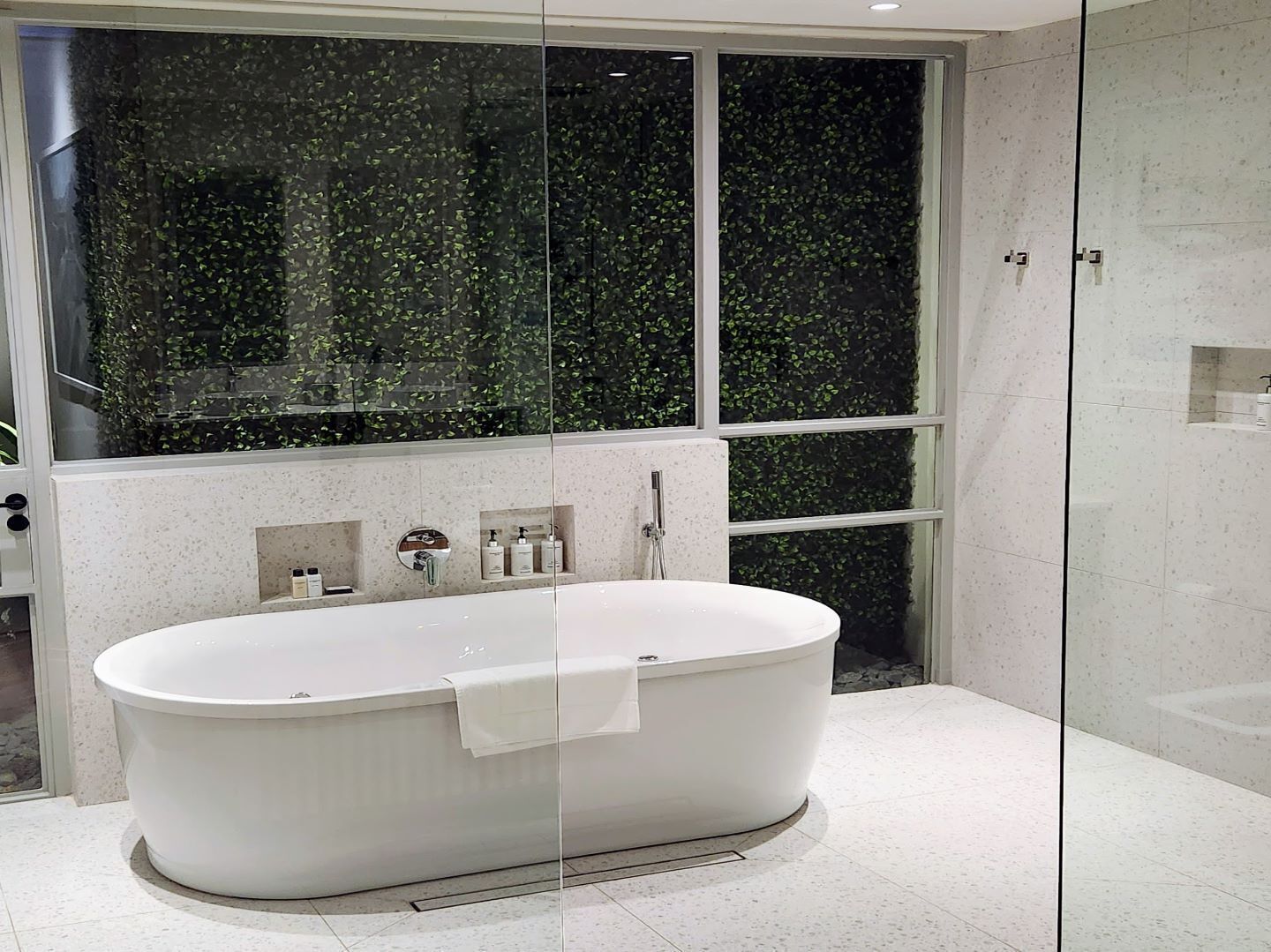 Un baño moderno con una bañera independiente, ducha con mampara de vidrio y un amplio ventanal con vistas a zonas verdes.