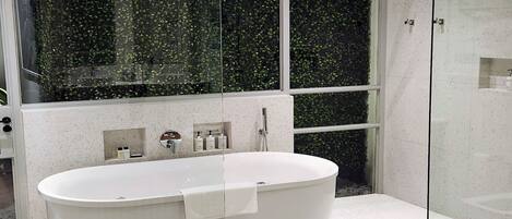 A modern bathroom with a freestanding bathtub, a glass-enclosed shower, and a large window with a view of greenery.