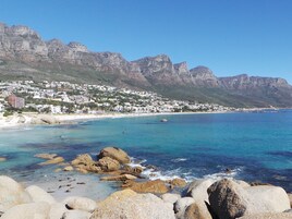 A coastal town with rocky shores, clear blue waters, and a backdrop of mountains.