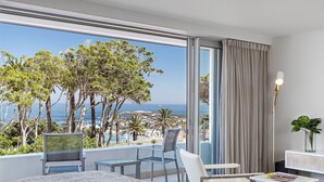 Une chambre d’hôtel dotée d’une grande fenêtre donnant sur la mer et les arbres.