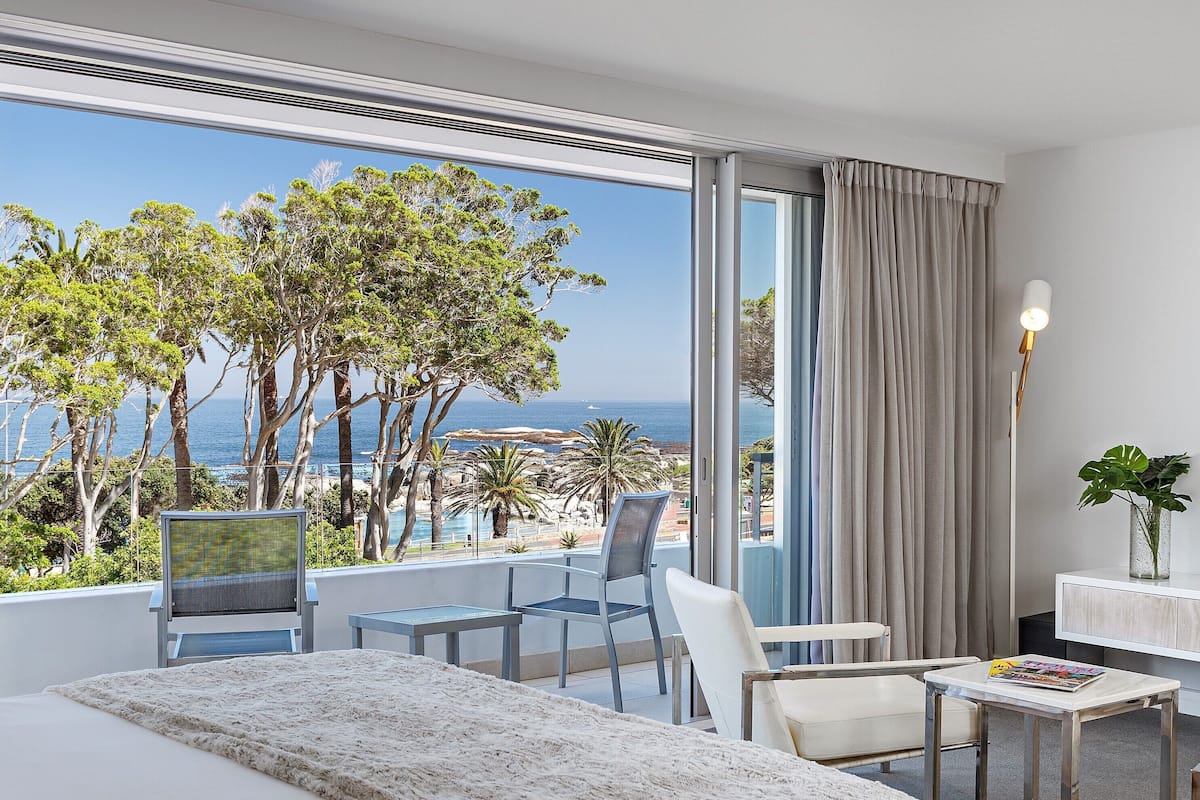 A hotel room with a large window offering a view of the sea and trees.
