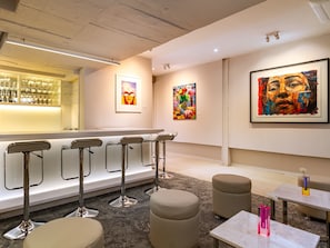 A modern bar area with bar stools, a counter with glasses, and artwork on the walls.