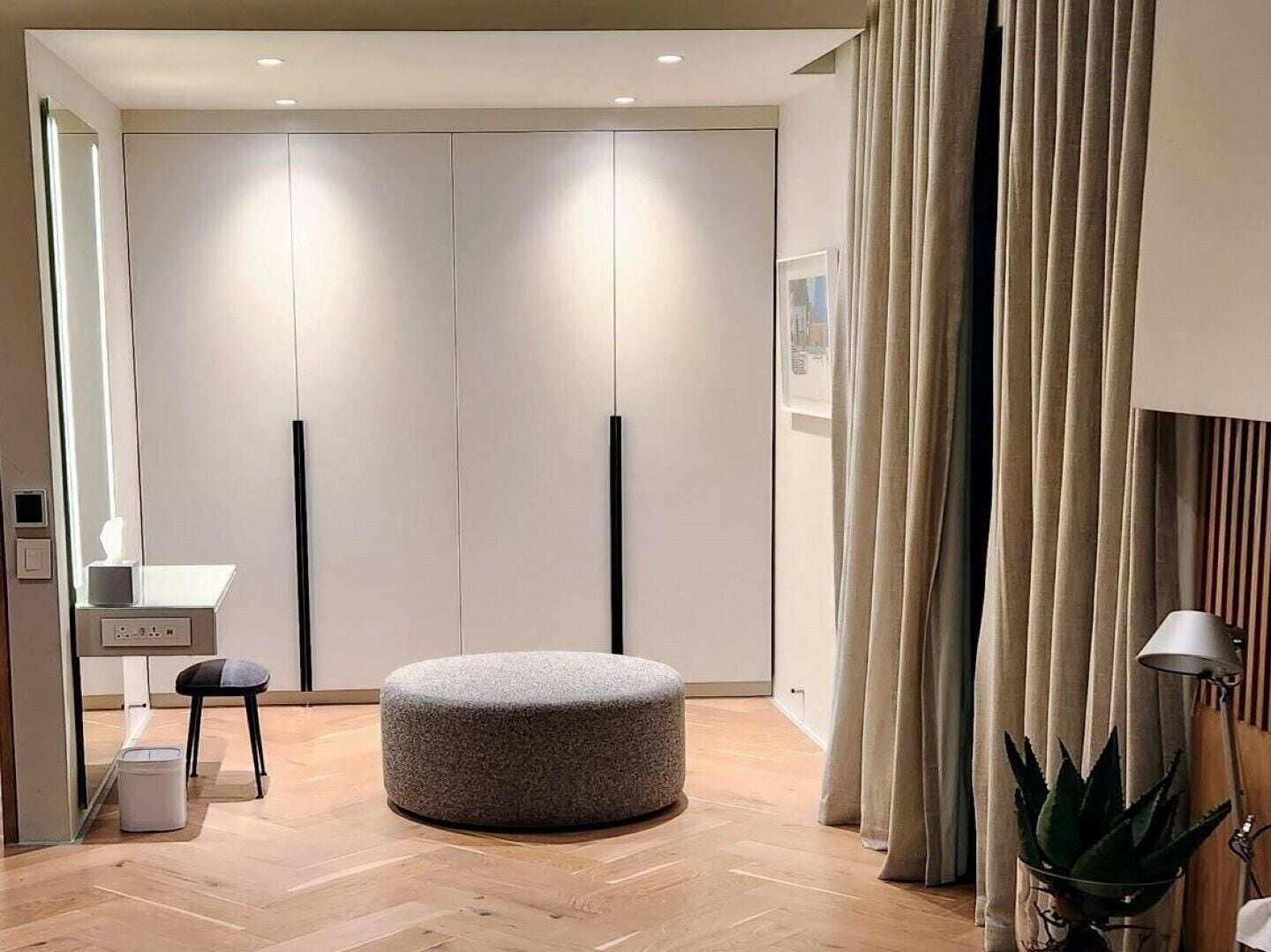 Une chambre moderne avec un plancher en bois, un pouf gris, un bureau avec une chaise et une armoire à portes coulissantes.