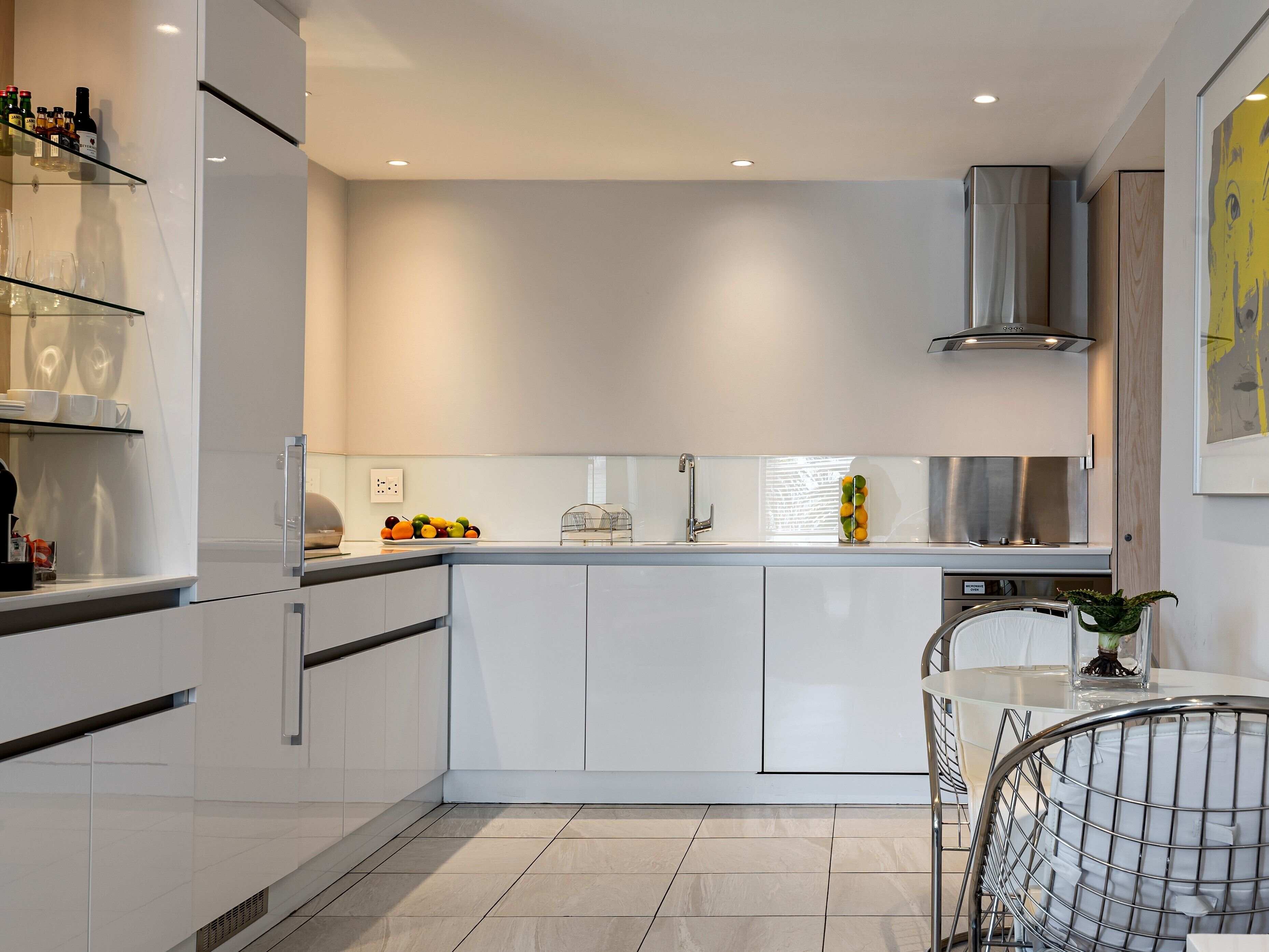 A modern kitchen with white cabinetry, a stainless steel range hood, and a glass island with fruit.