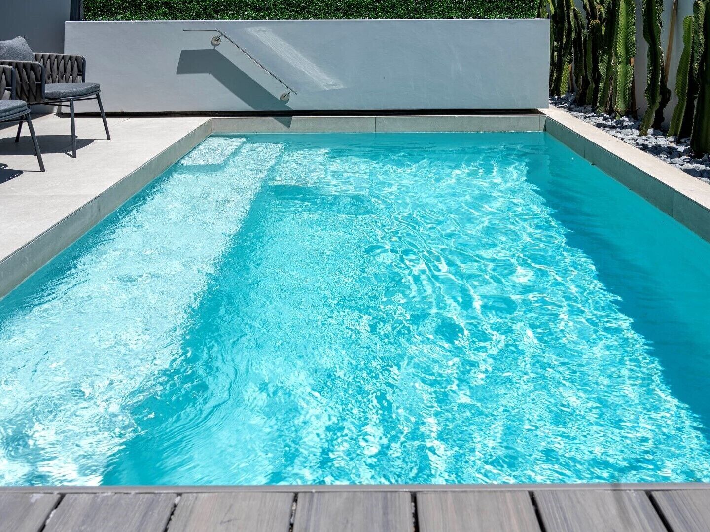A rectangular swimming pool with clear blue water, surrounded by a wooden deck and a low wall.