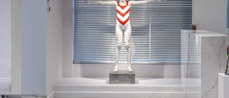 A statue of a swimmer in a white and red swimsuit on a pedestal in a modern lobby with a blue carpet and a large window with blinds.