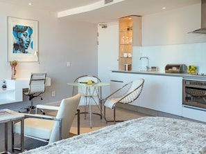 A modern kitchen with a dining area, a white sofa, and a framed artwork on the wall.