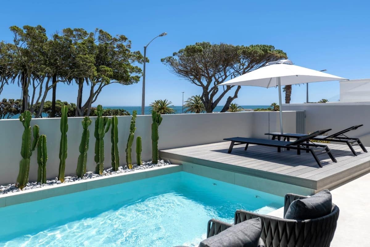 A pool area with a view of the sea, surrounded by cacti and trees.