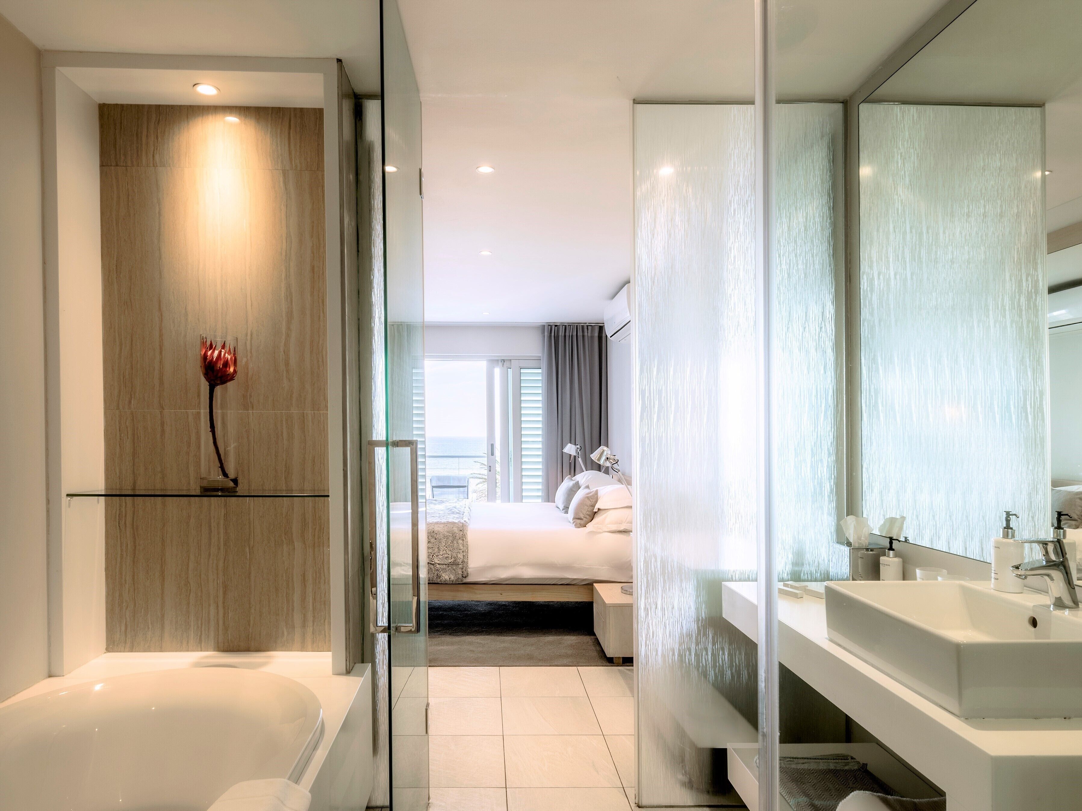 Een moderne hotelbadkamer met een douchecabine van glas, een grote spiegel en een witte wastafel.