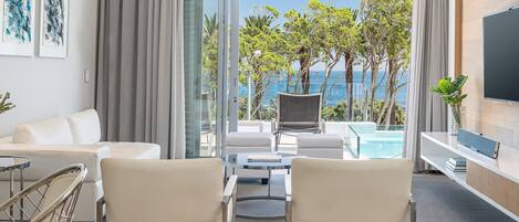 A modern hotel room with a balcony, a sofa, two armchairs, a TV, and a pool view.