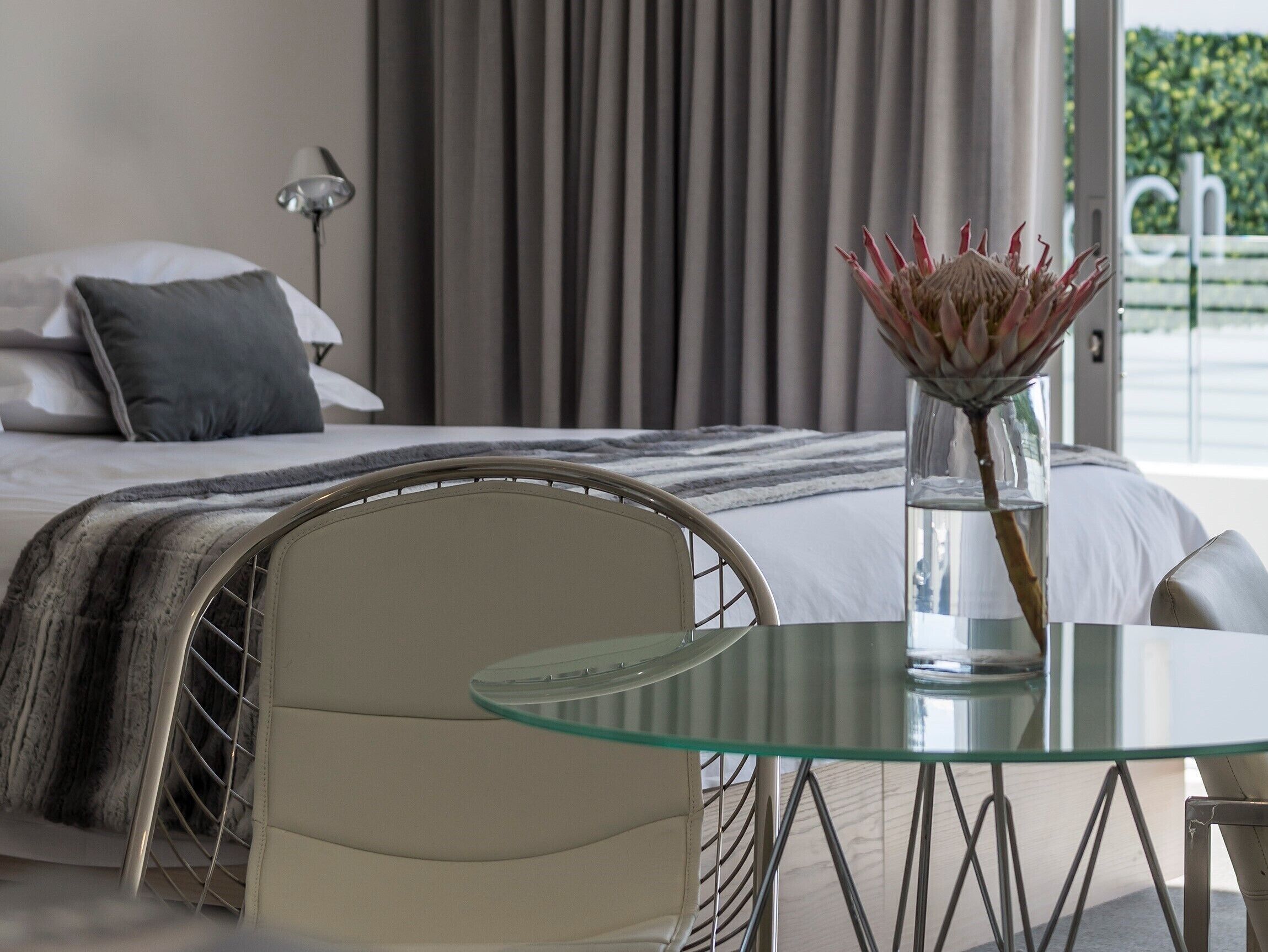 A modern bedroom with a bed, a glass table, and a chair.