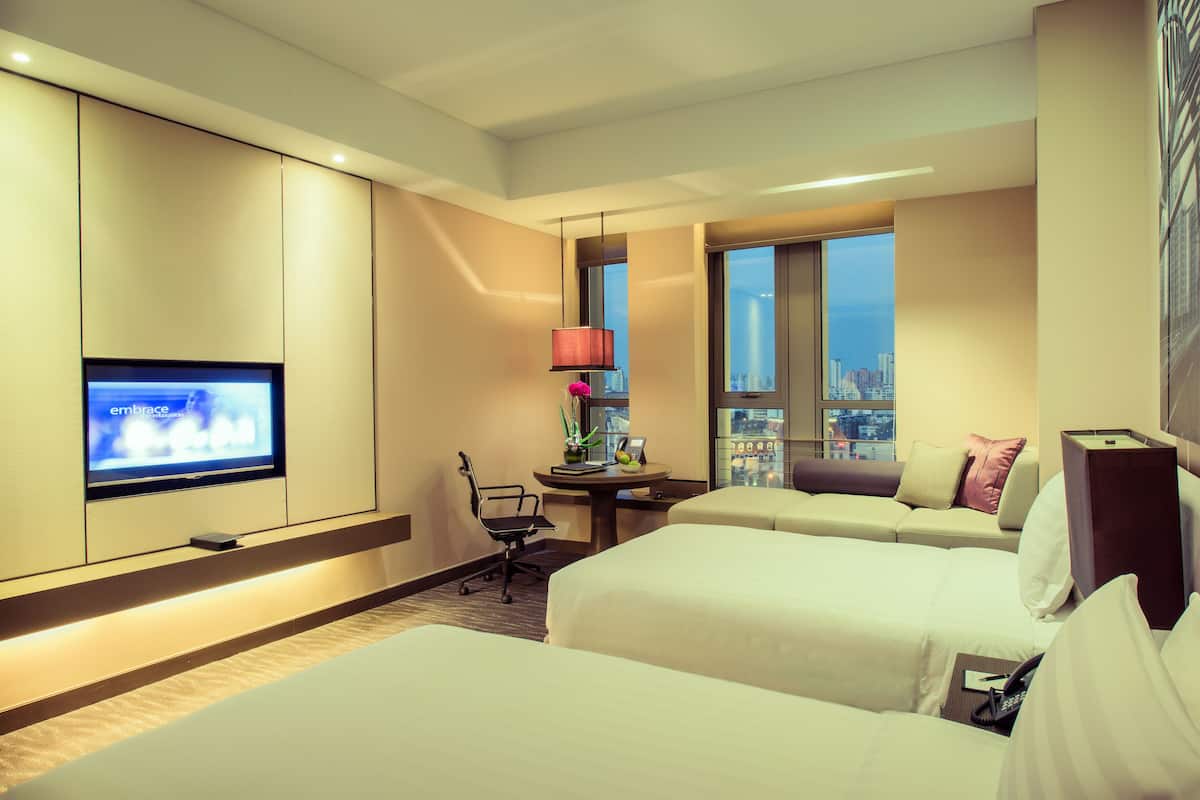 A hotel room with two beds, a desk, a chair, a TV, and a window with a city view.