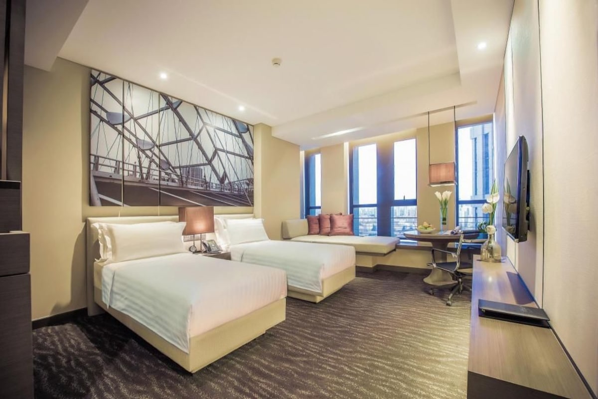 A hotel room with two beds, a desk, a chair, a TV, and a large window.