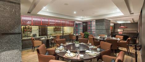 A modern dining area with round tables, wicker chairs, and a central decorative piece.