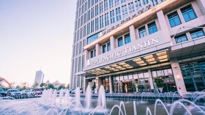 Un hotel con fachada moderna, una entrada destacada y una fuente de agua al frente.