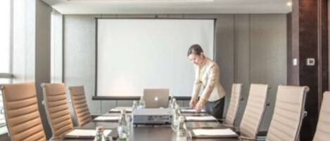 A conference room with a long table, multiple chairs, a laptop, water bottles, and a projector screen.