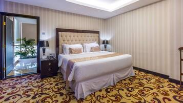 A hotel room with a large bed, a nightstand, a lamp, and a view of the outdoors through a door.