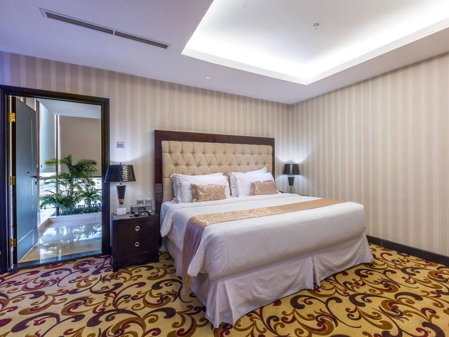 A hotel room with a large bed, a nightstand, a lamp, and a view of the outdoors through a door.