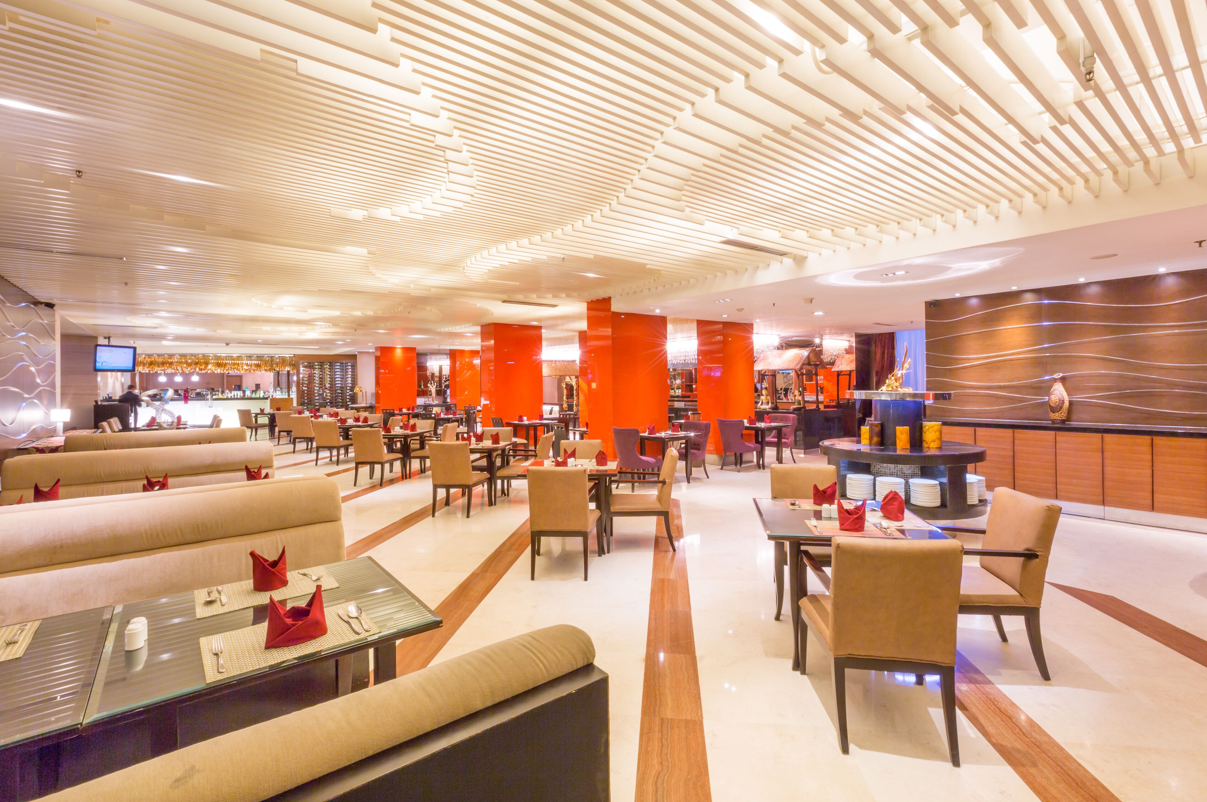 A modern hotel lobby with a central bar, seating areas, and a patterned ceiling.