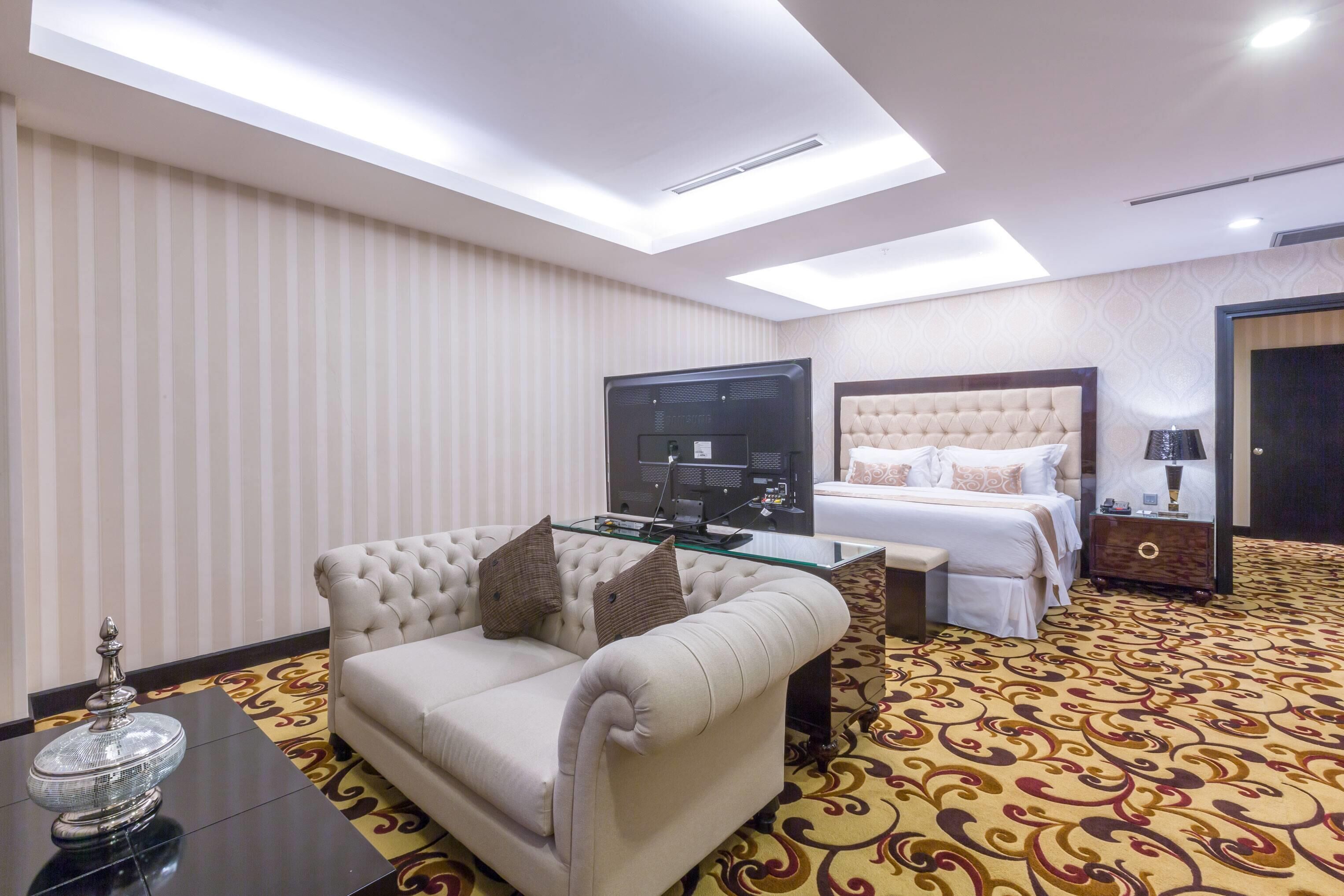 Una habitación de hotel con cama, sofá, televisor y lámpara decorativa.