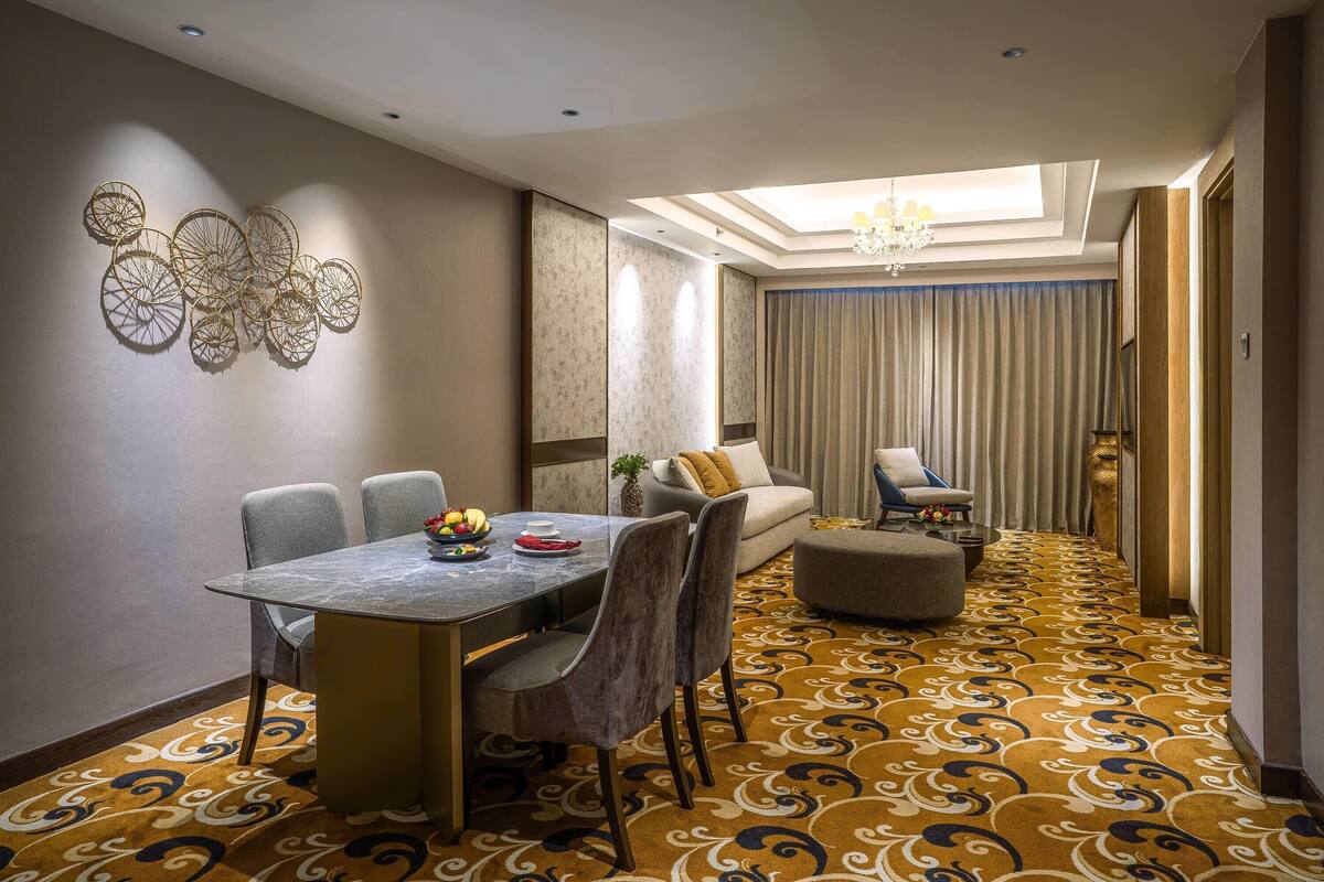 Habitación de hotel con comedor, sofá, sillón, alfombra estampada y candelabro.