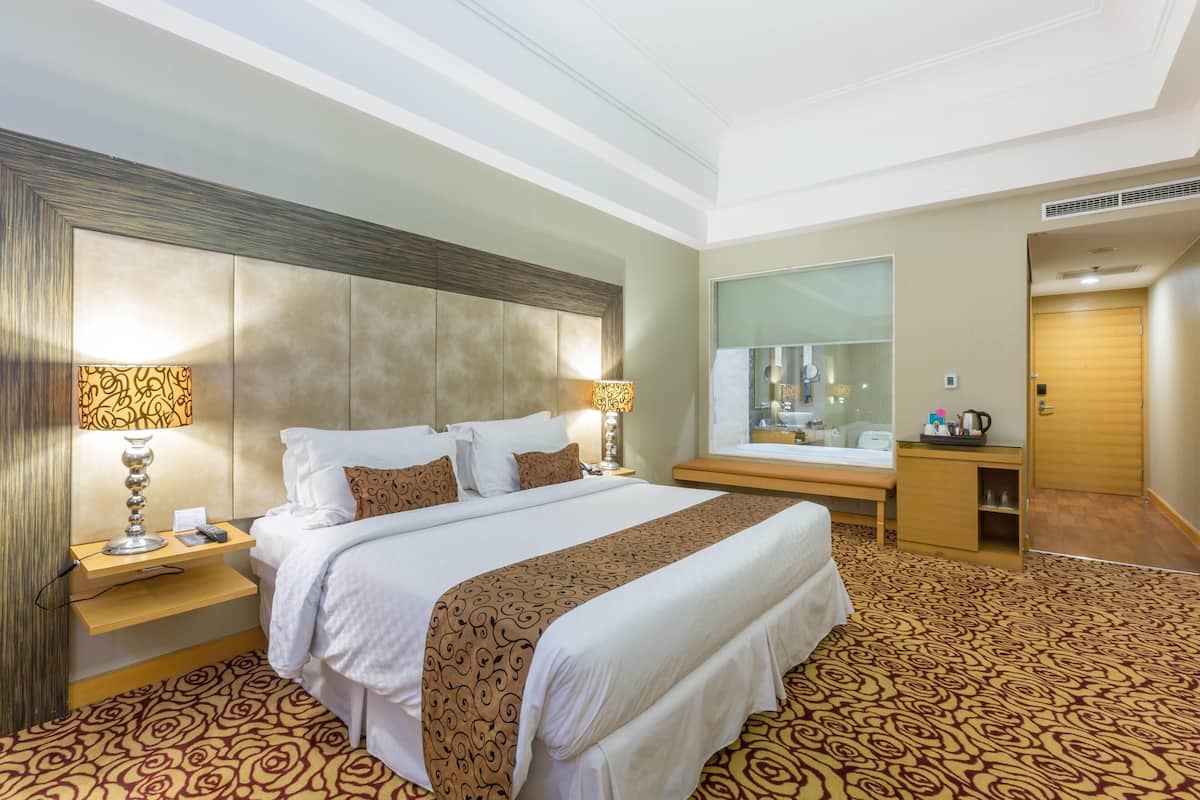 Habitación de hotel con una cama grande, dos mesitas de noche con lámparas, un armario de madera y un espejo en la pared.