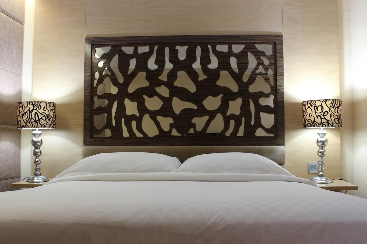 Una habitación de hotel con una cama grande, dos mesitas de noche con lámparas y un cabecero decorativo.
