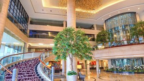 Un atrio de varios niveles con una escalera central, un árbol grande y un techo decorativo.