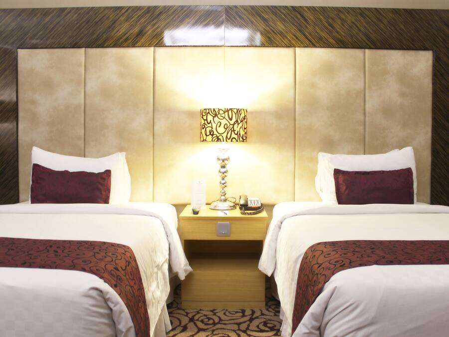 Habitación de hotel con dos camas, una mesita de noche con lámpara y una obra de arte en la pared.