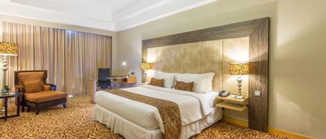 A hotel room with a large bed, a chair, a desk, and a television.