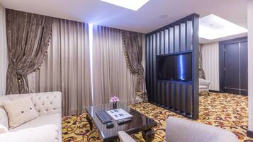 Habitación de hotel con sofá, sillón, una mesita de vidrio con un control remoto, televisión y alfombra estampada.