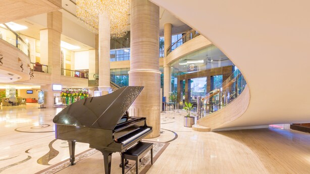 Un piano de cola imponente en un amplio vestíbulo con techos altos, una columna central y una escalera moderna.