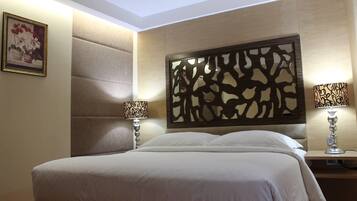 Ein Hotelzimmer mit einem großen Bett, zwei Nachttischlampen, einem dekorativen Kopfteil und einem gerahmten Bild an der Wand.
