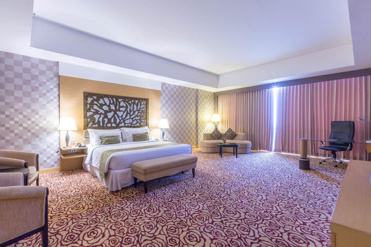 Una habitación de hotel con una cama grande, un escritorio, una silla, un sofá y una alfombra estampada.