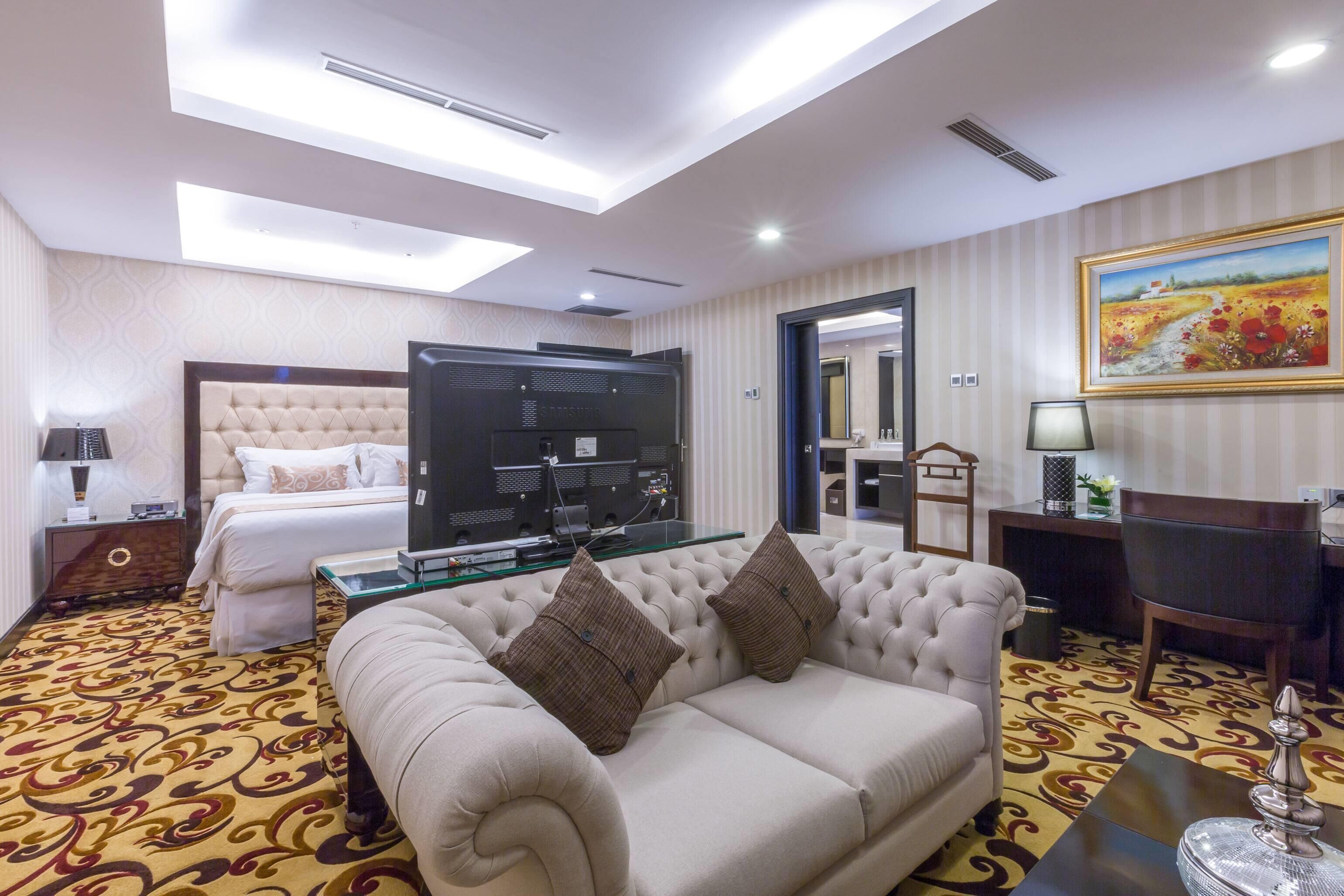 A hotel room with a large bed, a sofa, a TV, and a dining area.