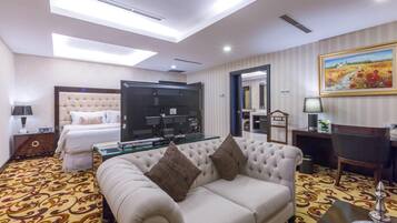 A hotel room with a large bed, a sofa, a TV, and a dining area.