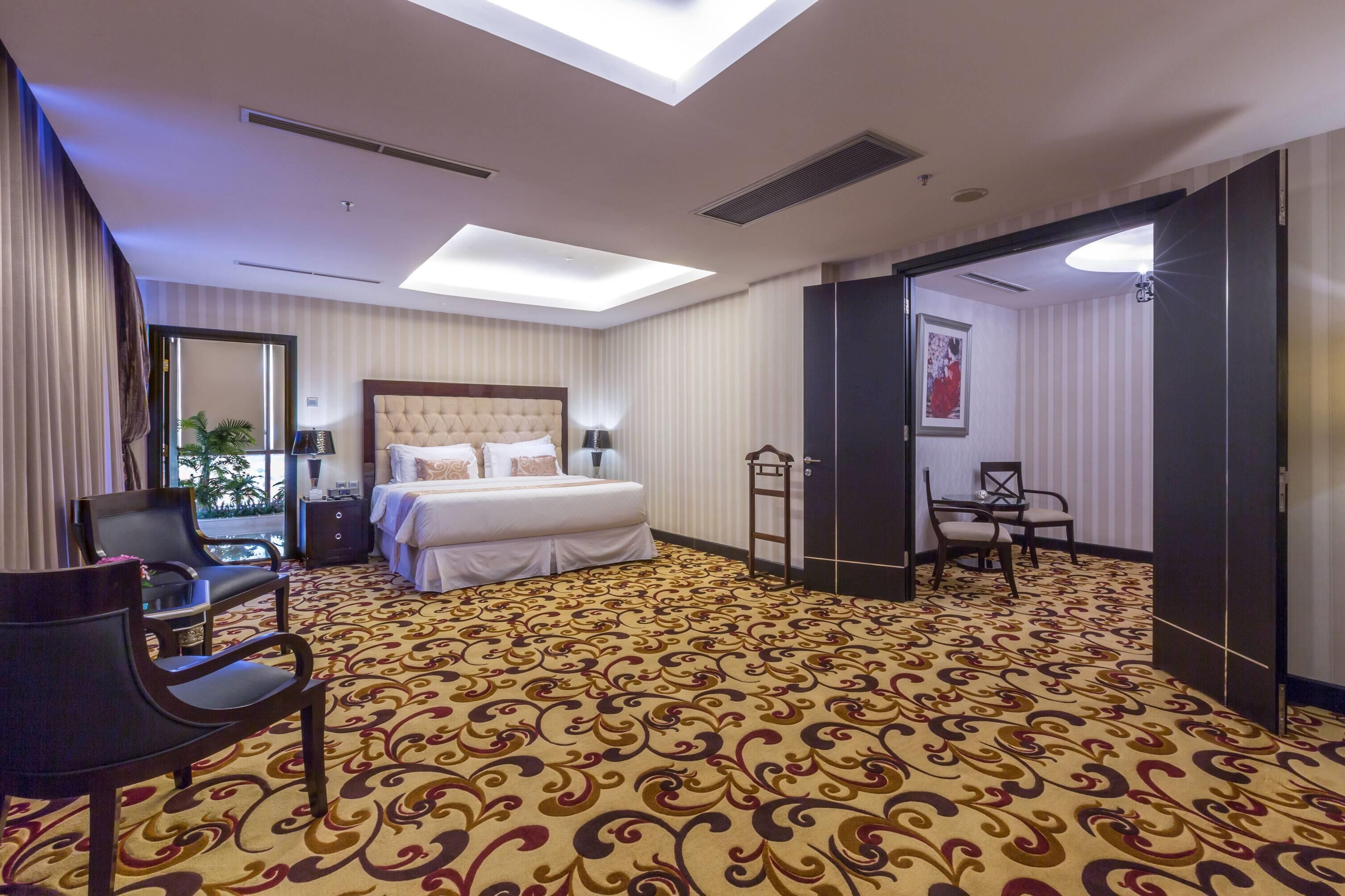 A hotel room with a large bed, a sitting area with a chair, a desk, and a mirror.