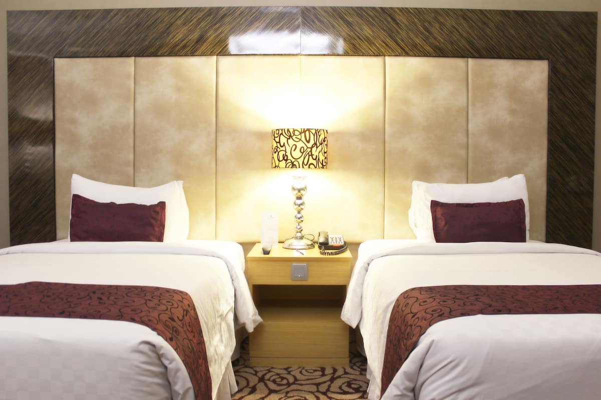 Una habitación de hotel con dos camas, una mesita de noche con lámpara, un teléfono y una obra de arte colgada en la pared.