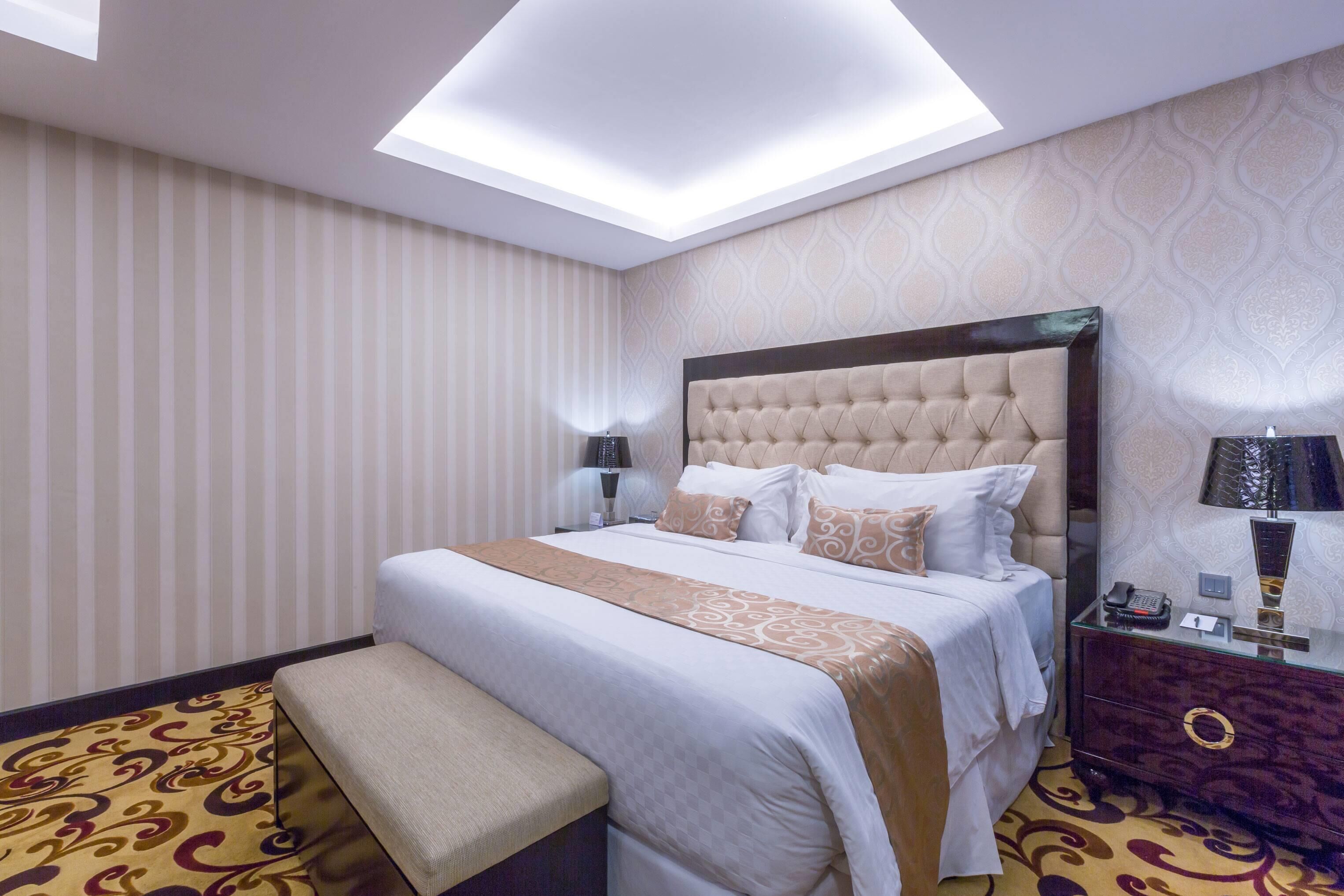 Une chambre d’hôtel avec un grand lit, une banquette, une table de chevet avec une lampe et un luminaire au plafond.