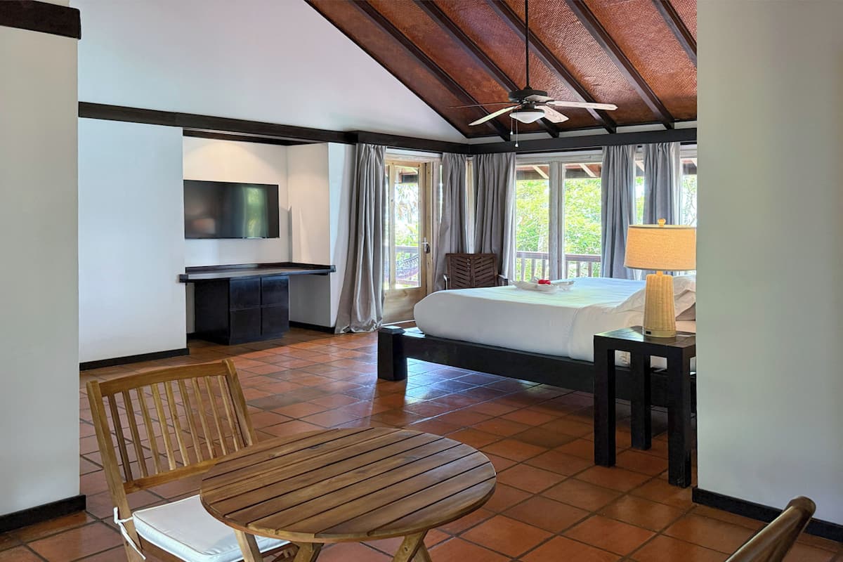 A hotel room with a bed, a desk, a chair, a TV, and a ceiling fan.