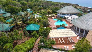 Un complex turístic amb diversos edificis de teulada de palla, una piscina central i gandules.