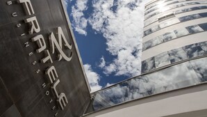 A modern building with a reflective glass facade and a clear sky with clouds. - Fratele Business (Patos de Minas)