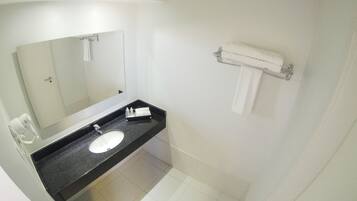 Un baño con lavamanos blanco, un espejo, toallero y secador de pelo.