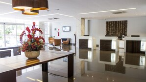 A modern reception area with a wooden reception desk, a potted plant, and a seating area with chairs. - Fratele Business (Patos de Minas)